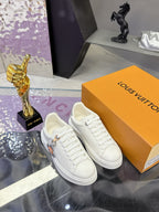 White Louis Vuitton lace-up sneakers with charm accents, displayed on orange boxes