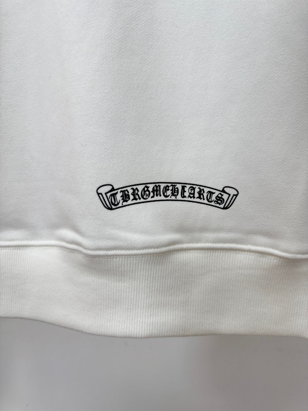 White hoodie close-up of small rectangular logo patch near hem