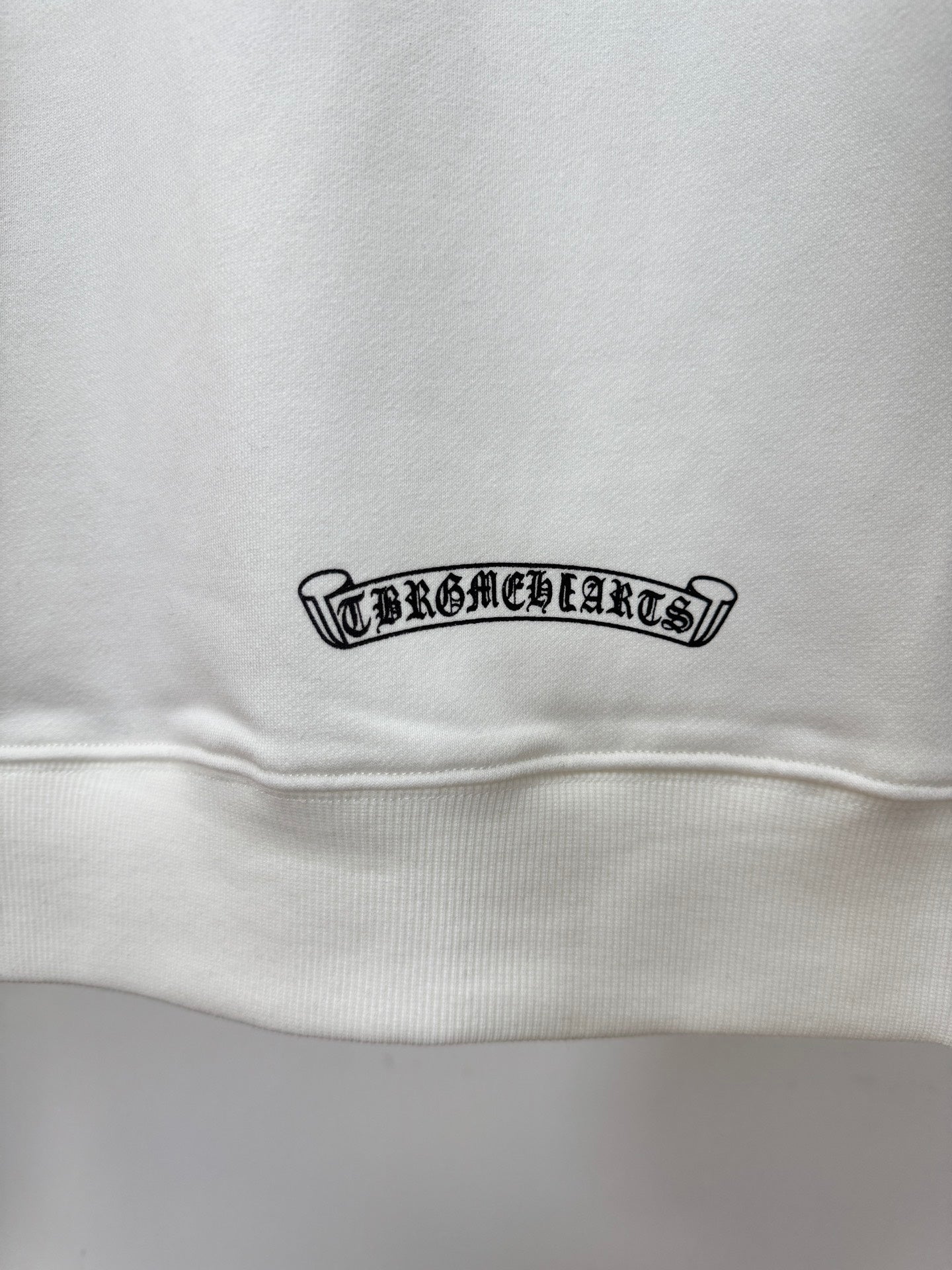 White hoodie close-up of small rectangular logo patch near hem