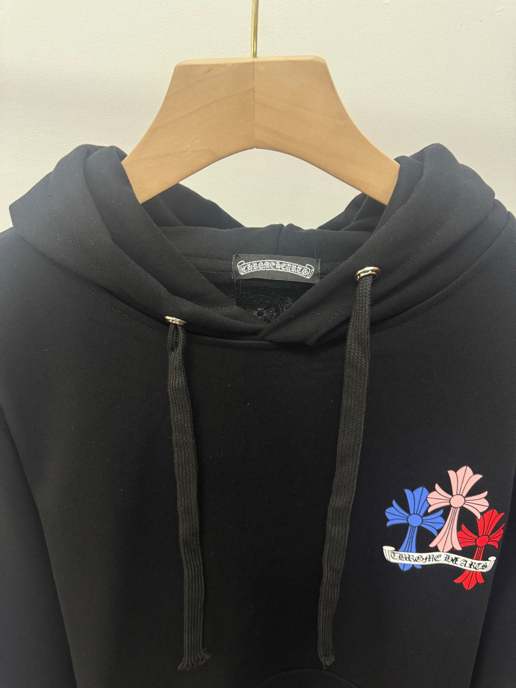 Black hoodie close-up with hood drawstrings and small floral chest graphic