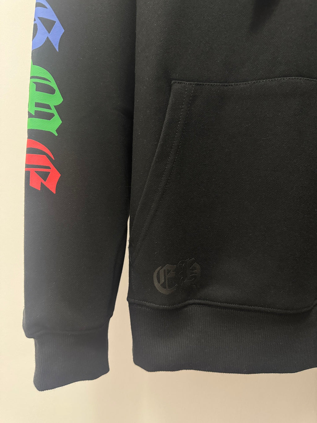Black hoodie sleeve and lower hem with small circular emblem near pocket