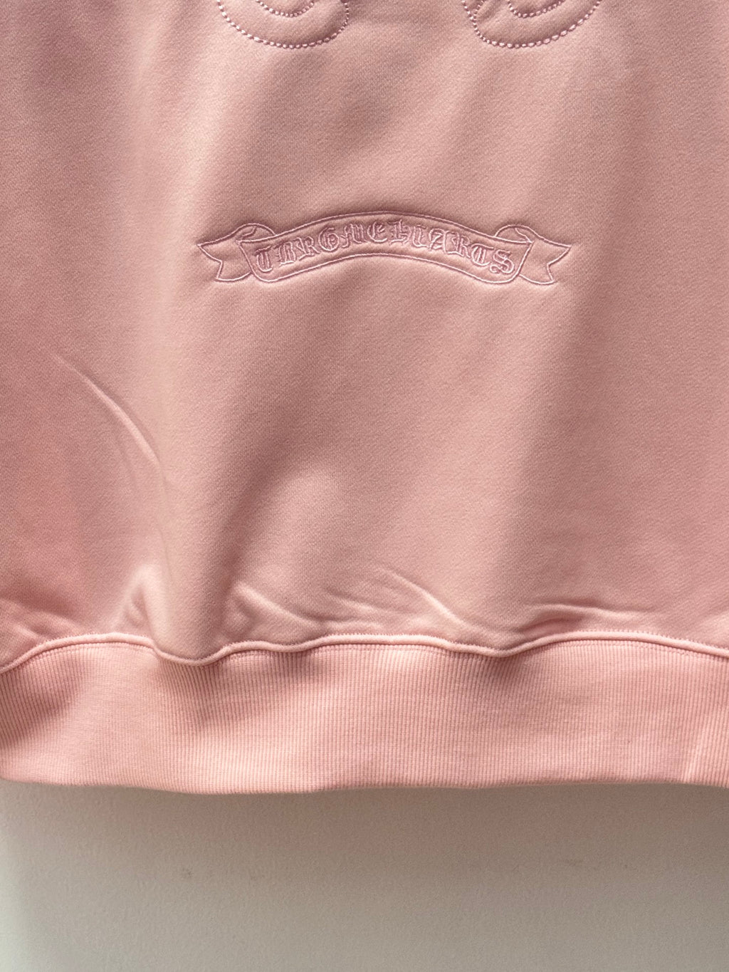 Light pink hoodie close-up of textured chest logo embroidery under the collar