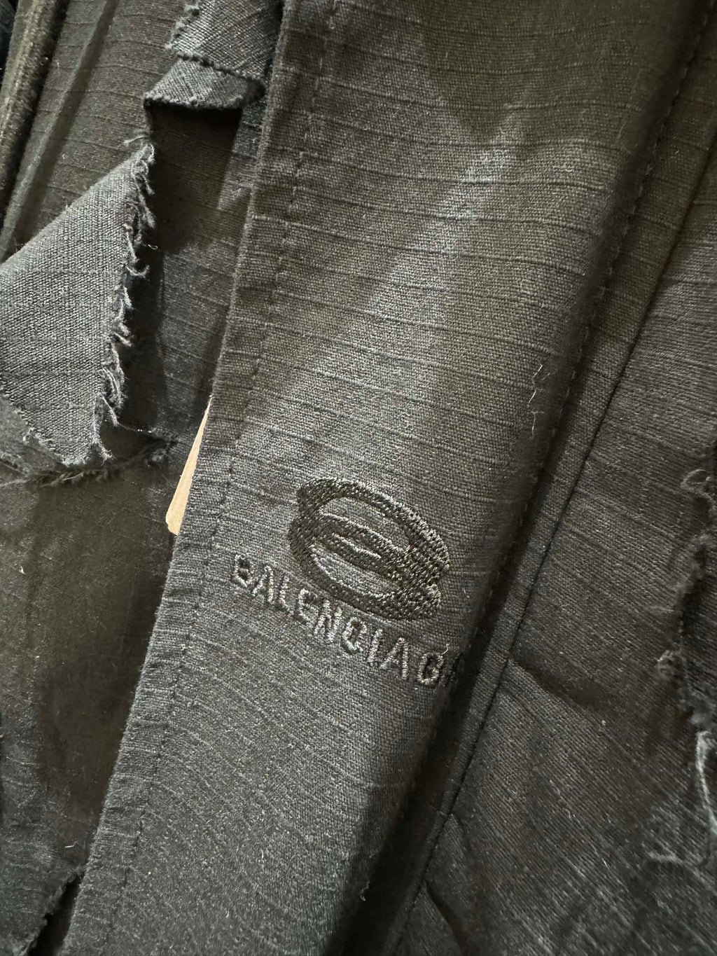 Balenciaga logo patch on dark long jacket with distressed fabric and seams