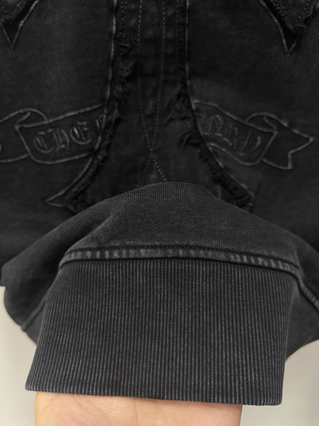 Dark hoodie cross embroidery detail with ribbed cuff at the bottom edge.