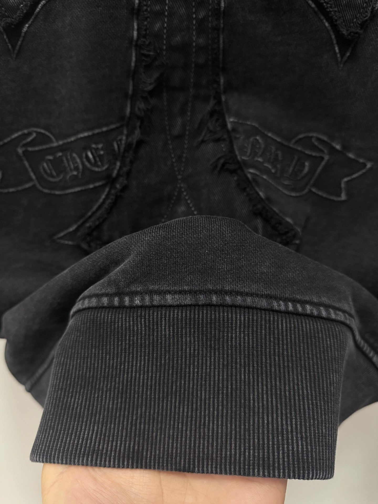 Dark hoodie cross embroidery detail with ribbed cuff at the bottom edge.