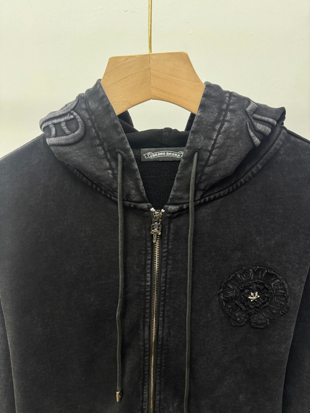 Dark zip-up hoodie close-up: hood, front zipper, drawstrings, and chest crest patch.