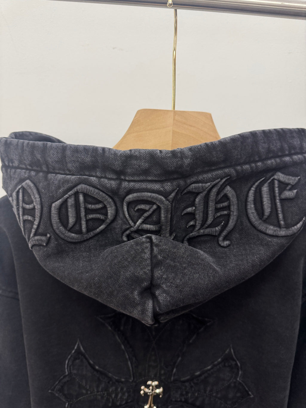 Dark hoodie back view close-up with large hood graphic and center cross emblem detail.