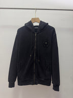 Dark zip-up hoodie with hood, drawstrings, front zipper, and small chest crest patch.