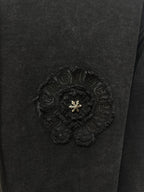 Dark hoodie chest badge patch with textured embroidery and small gold emblem in center.
