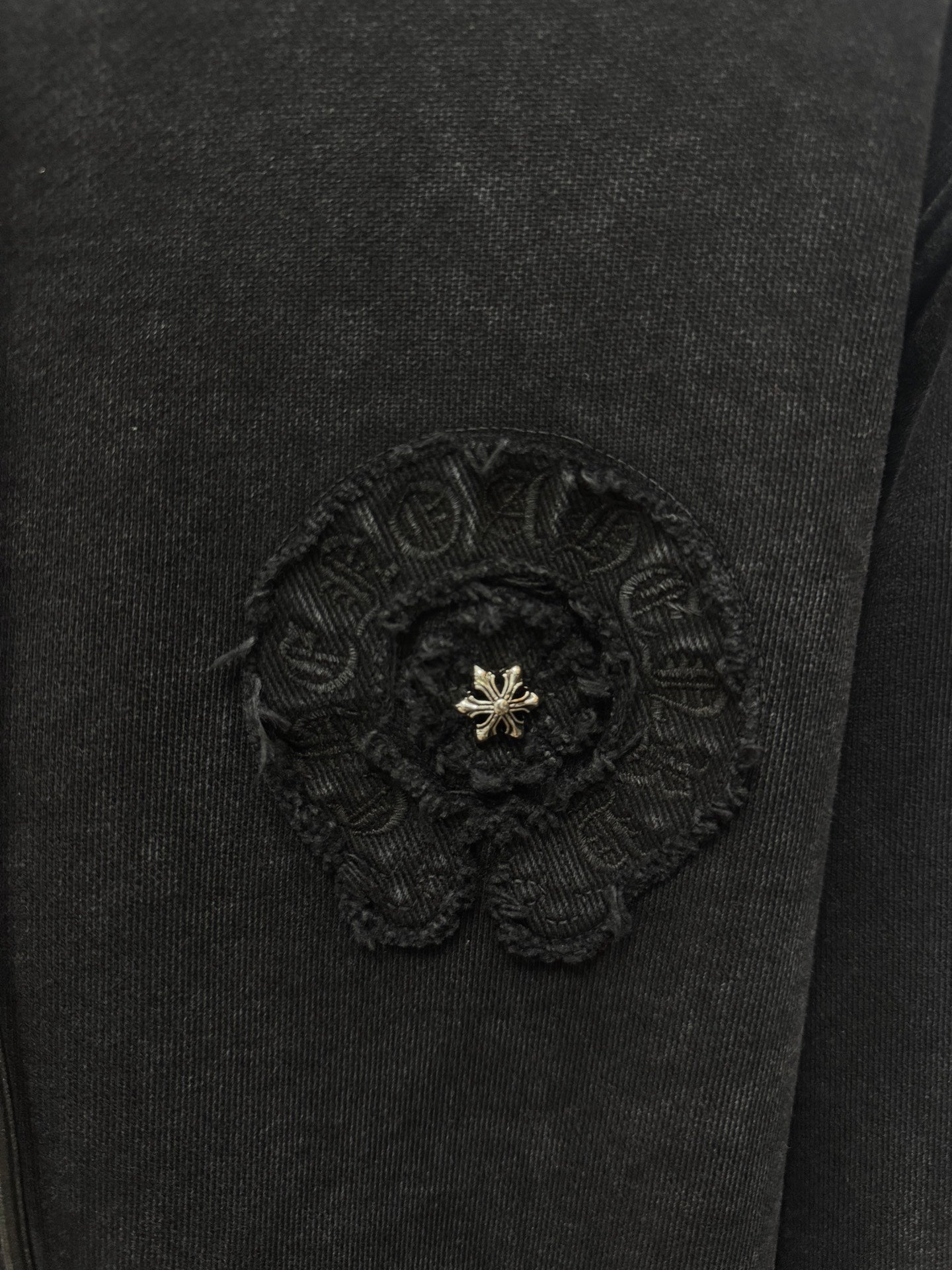 Dark hoodie chest badge patch with textured embroidery and small gold emblem in center.