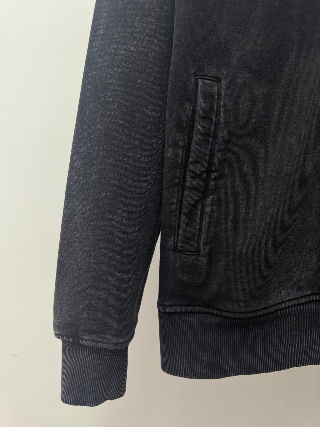 Dark zip-up hoodie sleeve and hem with ribbed cuffs and stitched pocket area.