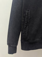 Dark zip-up hoodie sleeve and hem with ribbed cuffs and stitched pocket area.