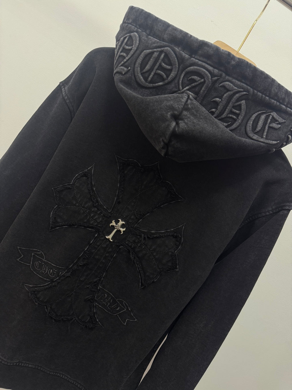 Dark hoodie close-up of hood graphic and cross emblem patch near the chest.