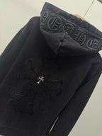 Dark hoodie close-up of hood graphic and cross emblem patch near the chest.