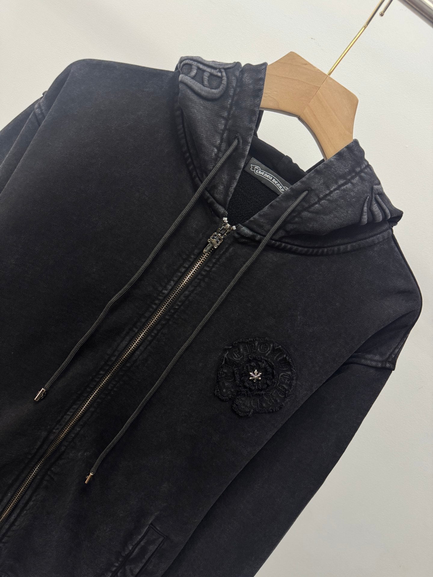 Dark zip-up hoodie side view with front zipper, drawstrings, and round chest emblem.