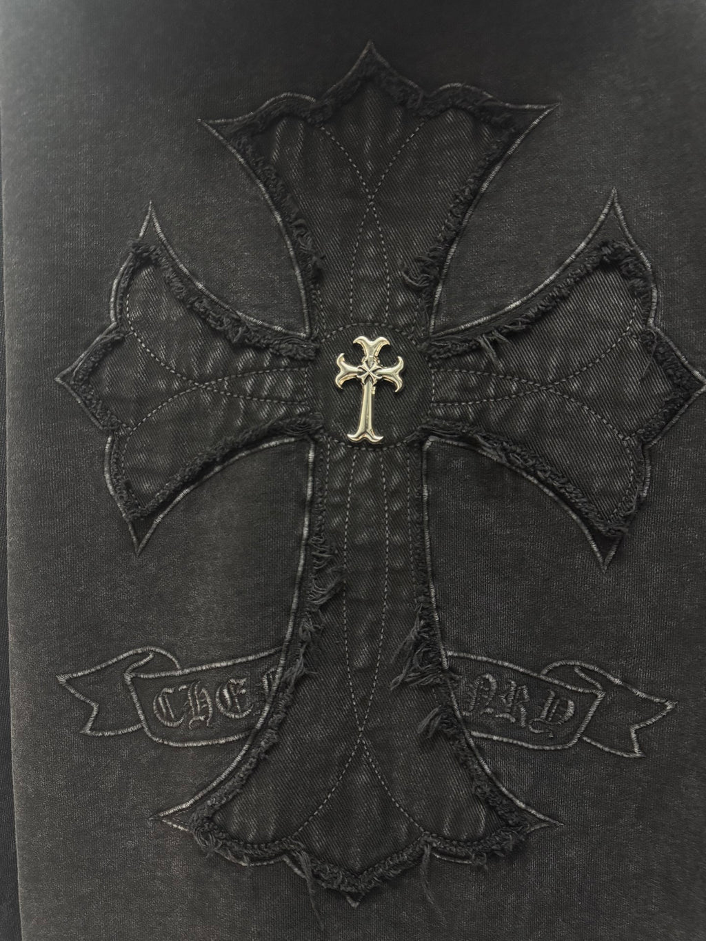 Dark hoodie back embroidery: large cross applique with gold emblem at the center.