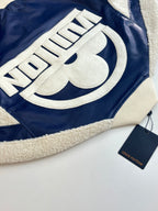 Close-up of cream embroidered logo lettering on navy jacket with sherpa trim