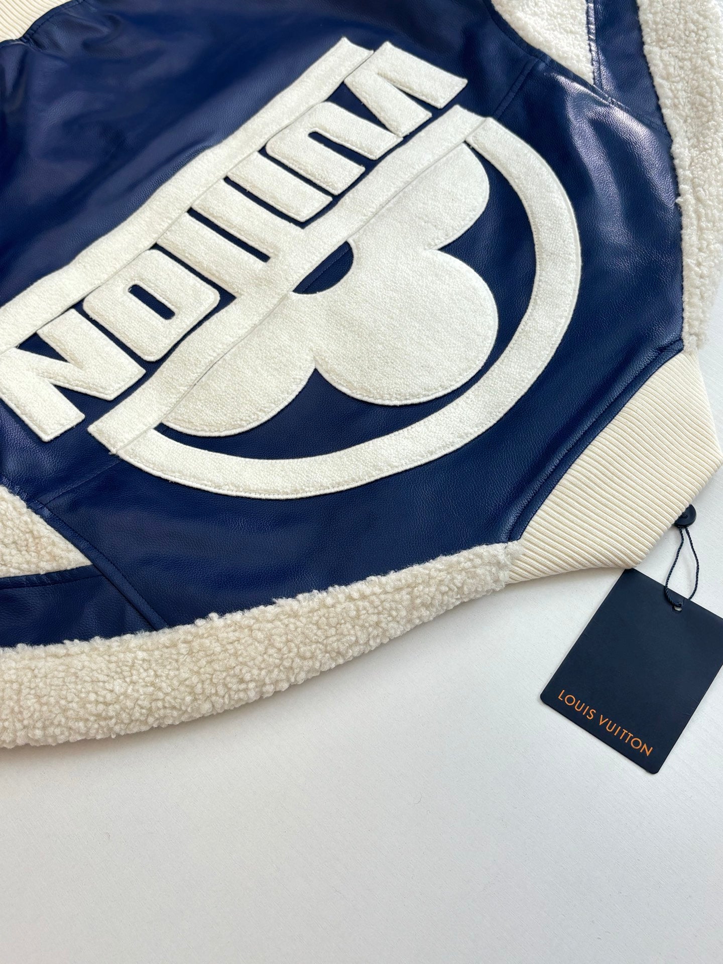 Close-up of cream embroidered logo lettering on navy jacket with sherpa trim