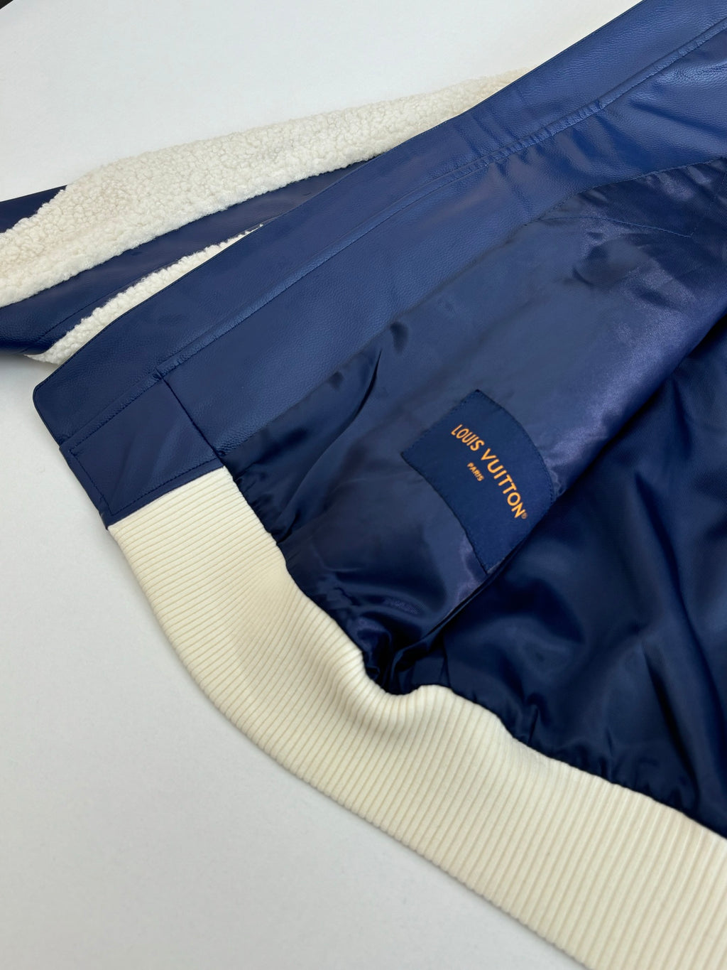 Back hem view of navy zip jacket with cream ribbed panels and small logo patch