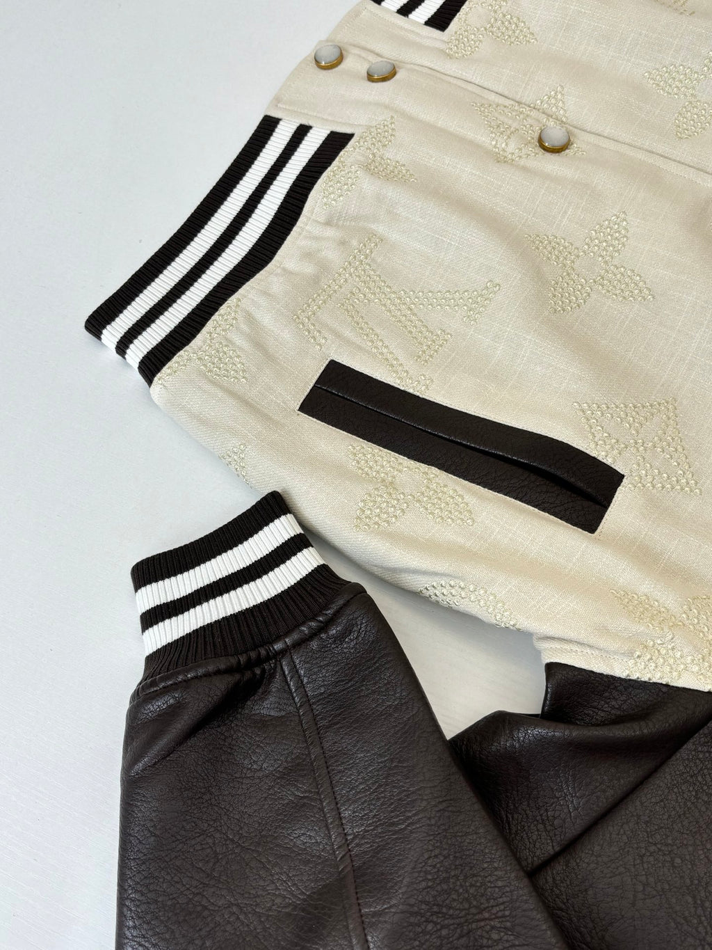 Louis Vuitton varsity jacket detail, cream cuffs with black-and-white stripes and gold snaps