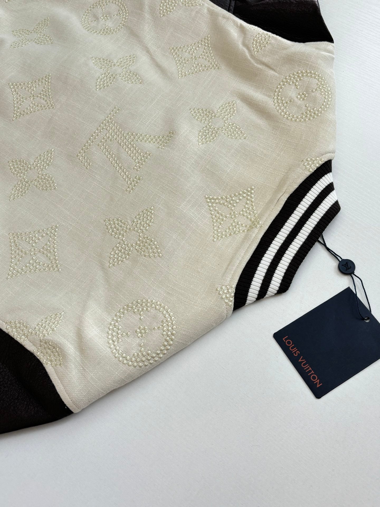 Louis Vuitton varsity jacket fabric close-up, cream textured knit with striped trim and tag