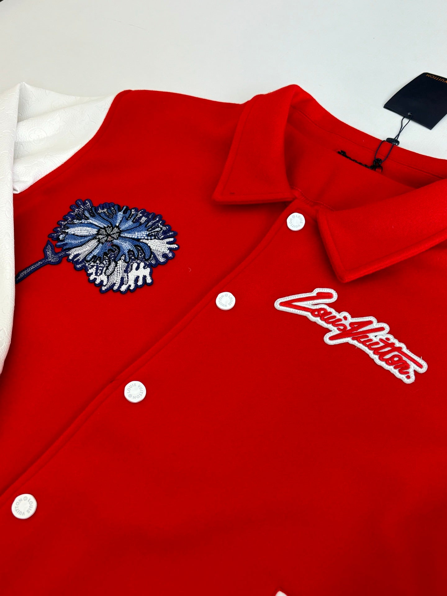 Red varsity jacket close-up with blue floral patch, Louis Vuitton script logo, and buttons