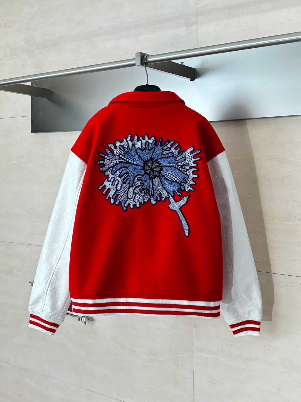 Red varsity jacket back with blue floral patch, ribbed hem, and white striped cuffs