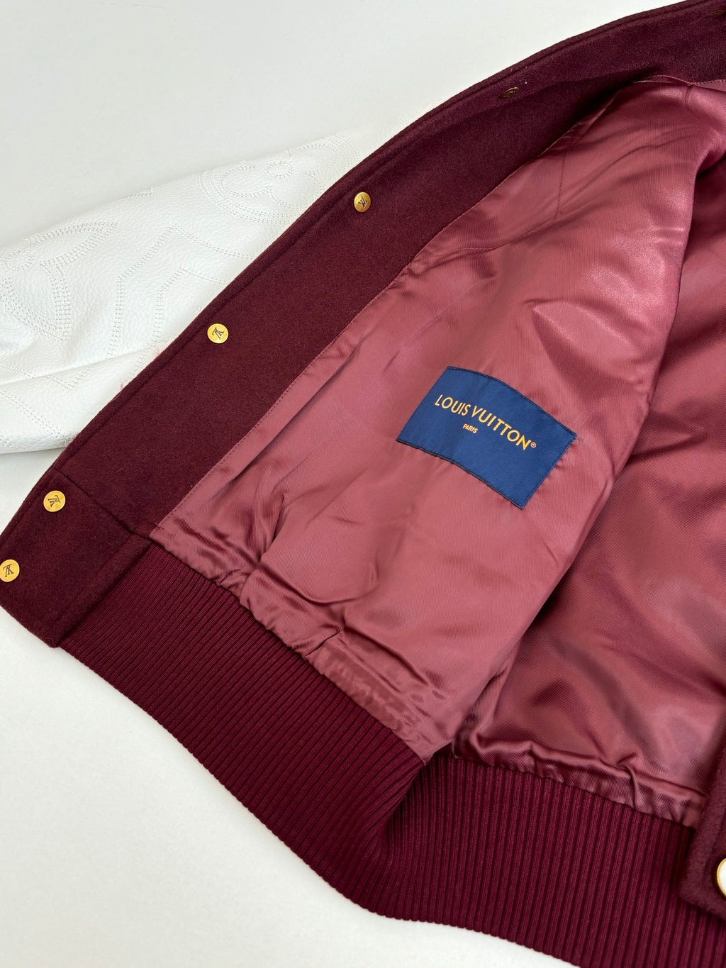 Inside view of burgundy jacket with pink lining and blue brand patch near cuff
