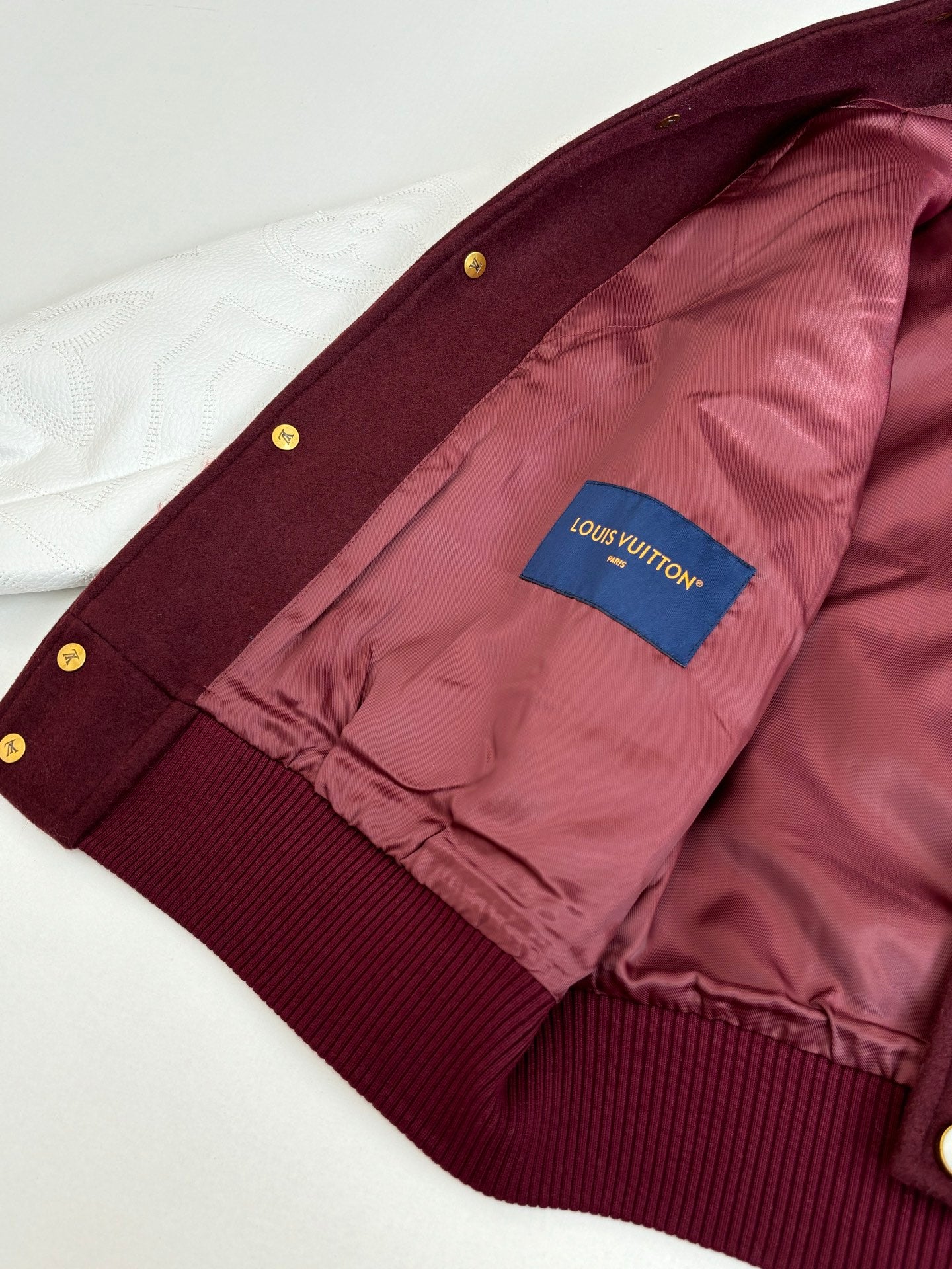 Inside view of burgundy jacket with pink lining and blue brand patch near cuff