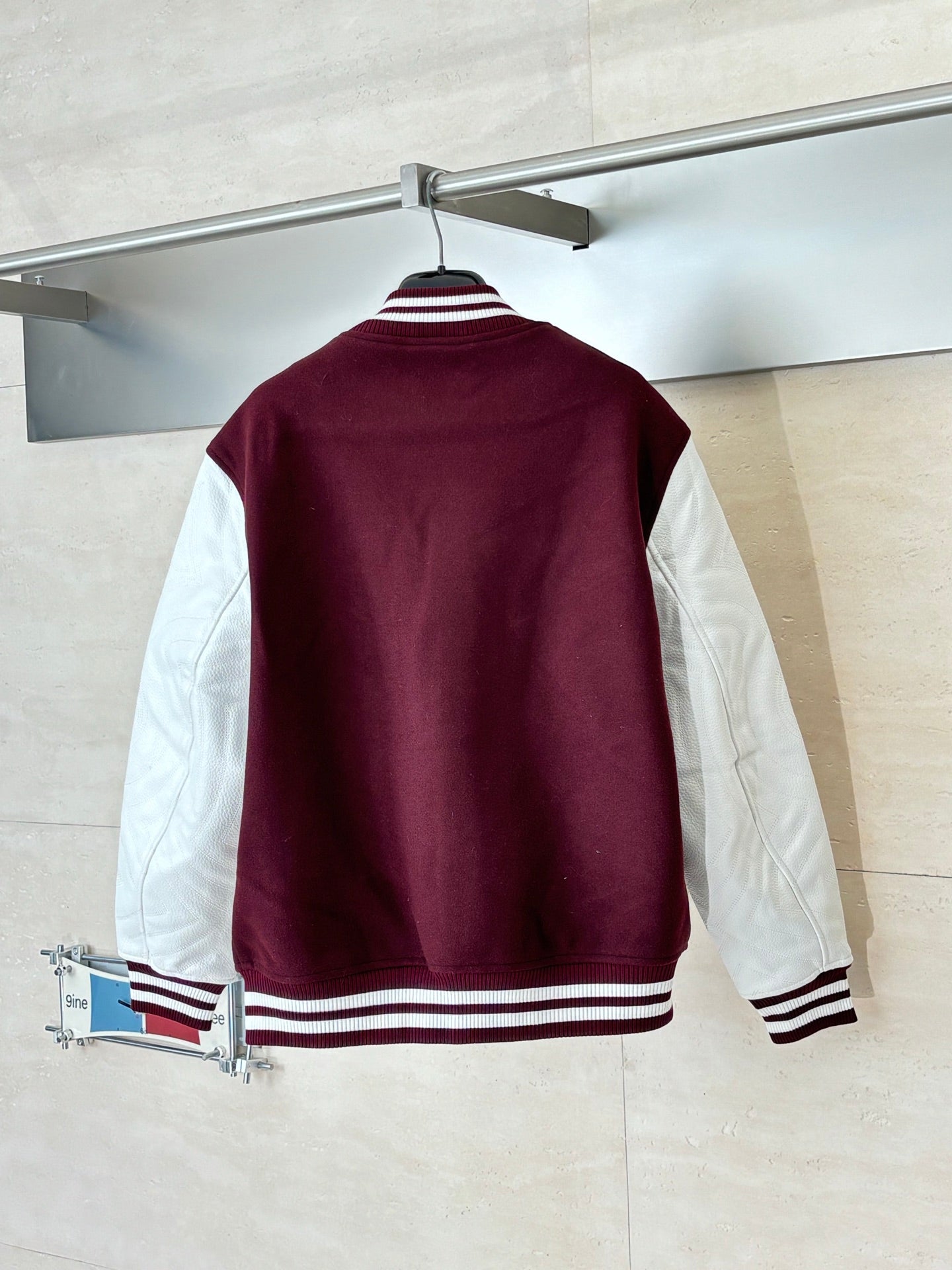Back view burgundy varsity jacket with white stripe trim at hem and cuffs