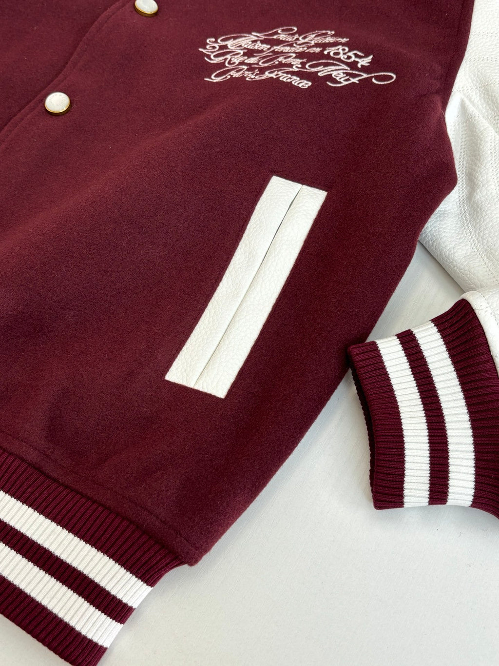 Close-up of burgundy varsity jacket sleeve stripe panel and front pocket/patch detail