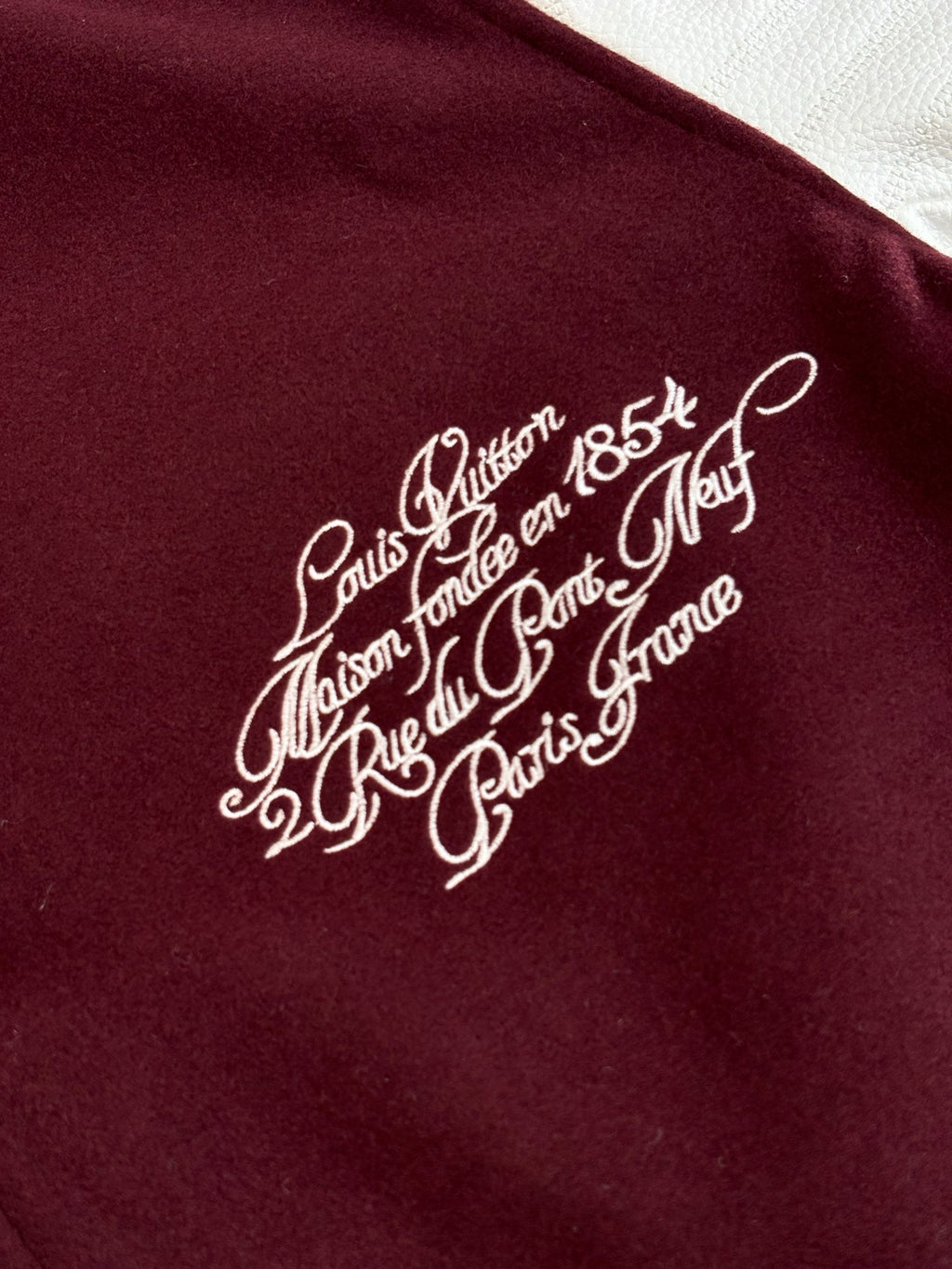 Close-up of white script logo on burgundy varsity jacket chest