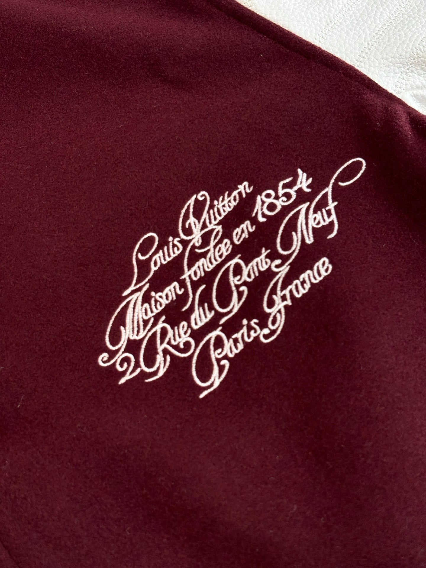 Close-up of white script logo on burgundy varsity jacket chest