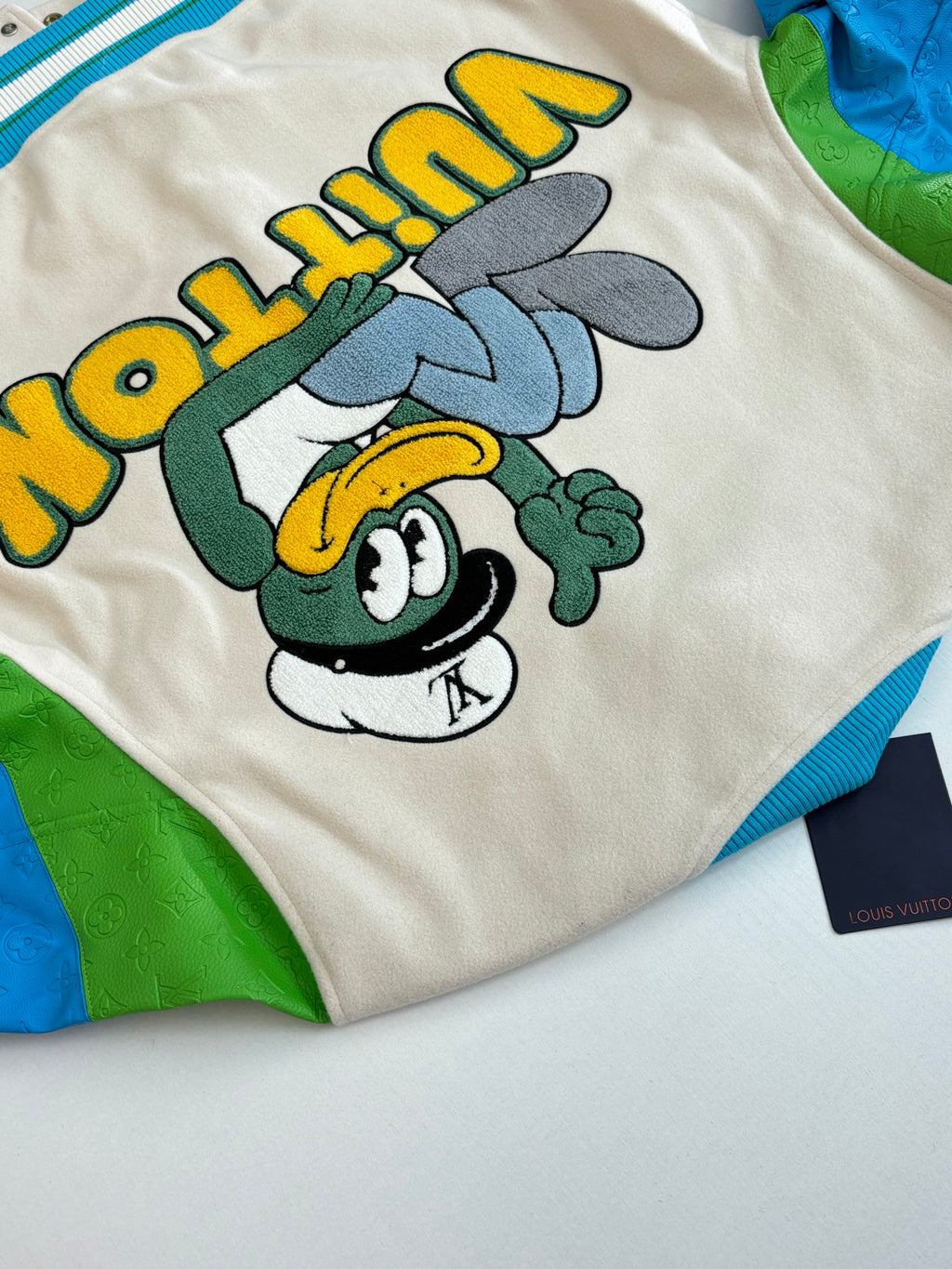 Louis Vuitton sleeve graphic on cream: character face with green and yellow accents