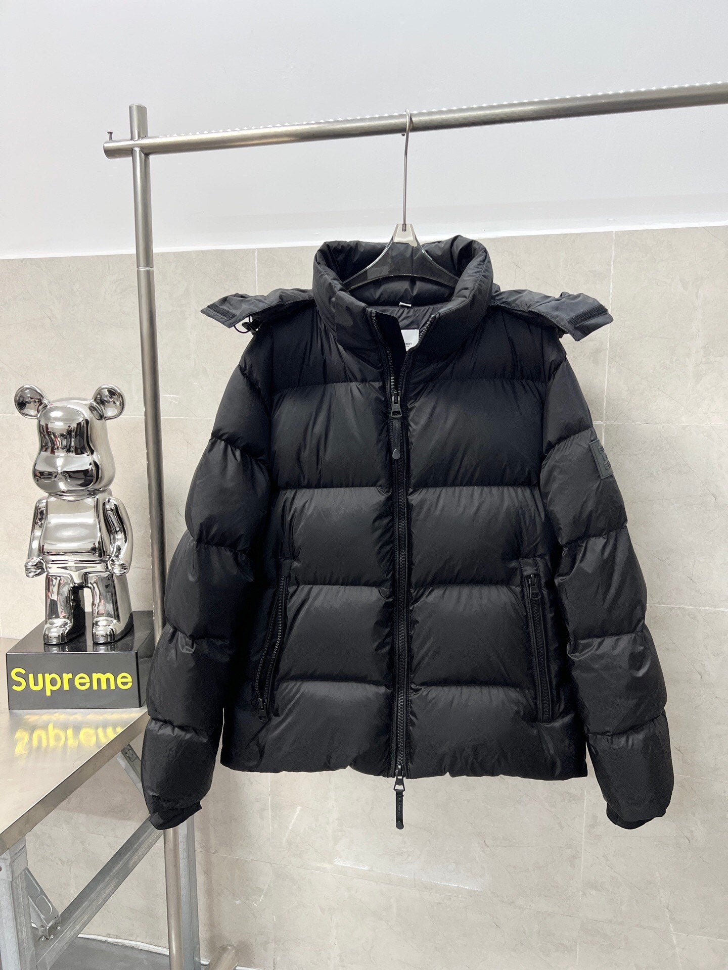 Long hooded puffer jacket, dark color, front view with stand collar and zipper pull
