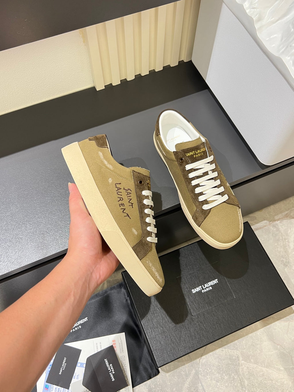 YSL unisex sneakers held in hand, tan with brown side panel and white laces