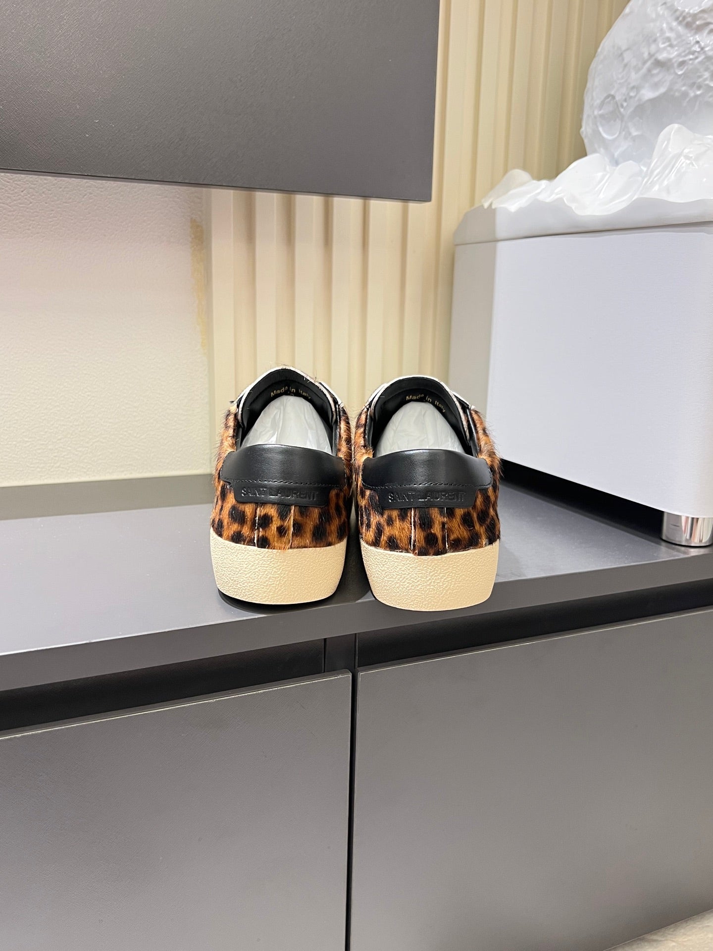 YSL leopard-print sneakers with black heel panels, back view on shelf