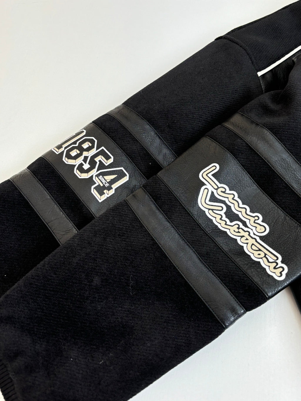 Louis Vuitton long jacket sleeve close-up, black with cream logo patches on striped band