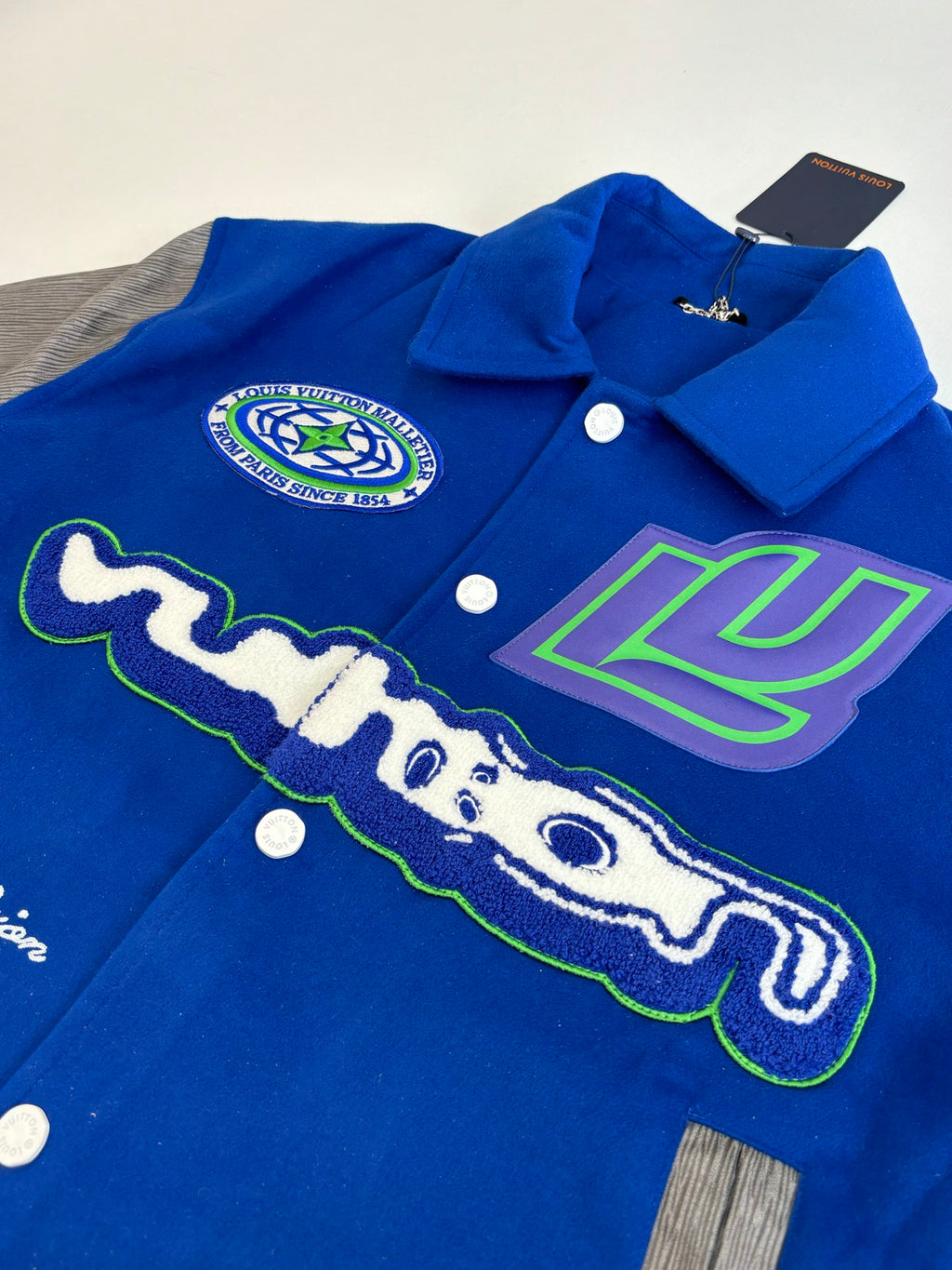 Blue varsity jacket close-up with Louis Vuitton crest and graffiti-style graphic