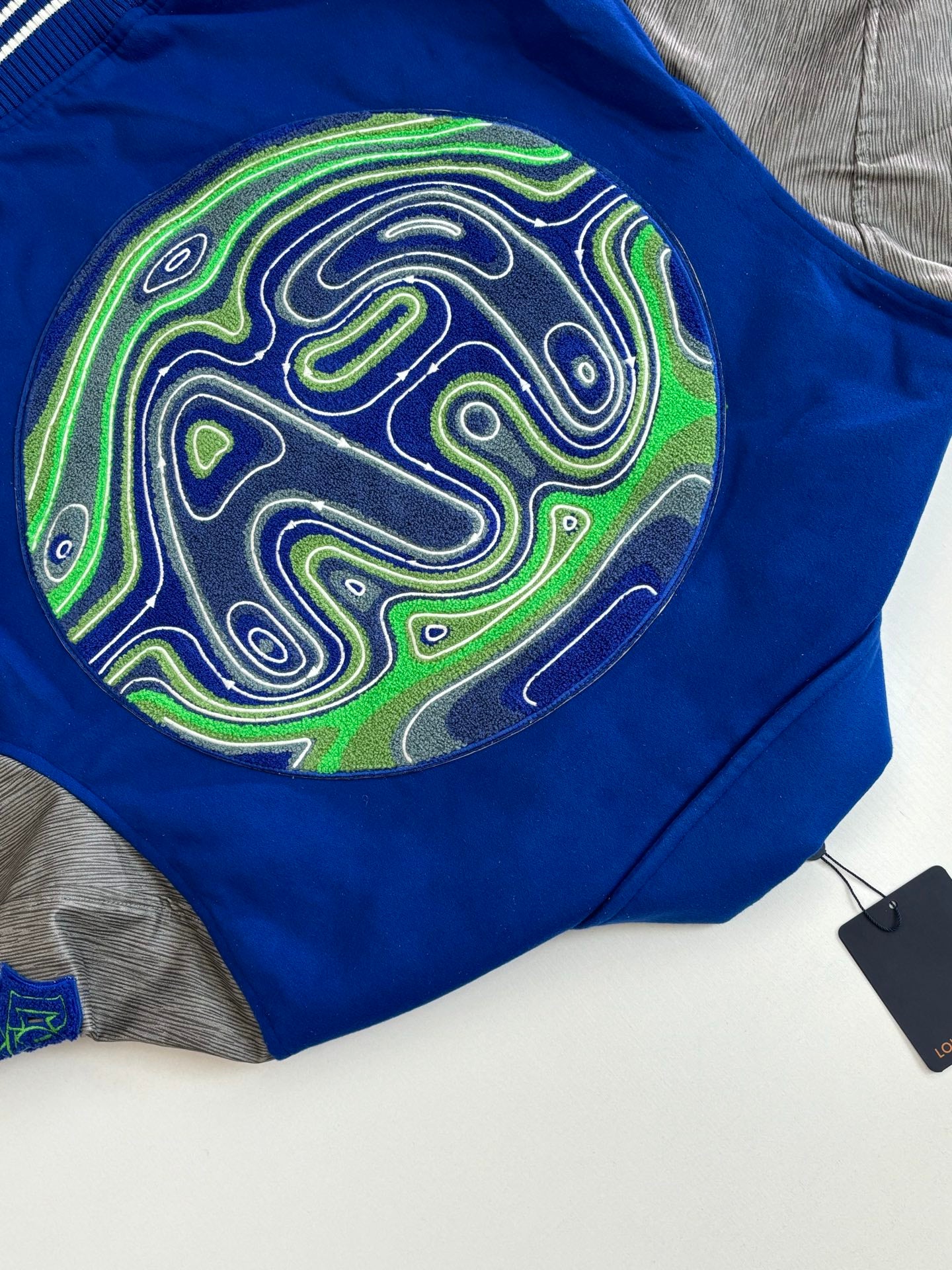 Blue varsity jacket patch detail with neon swirl artwork on front