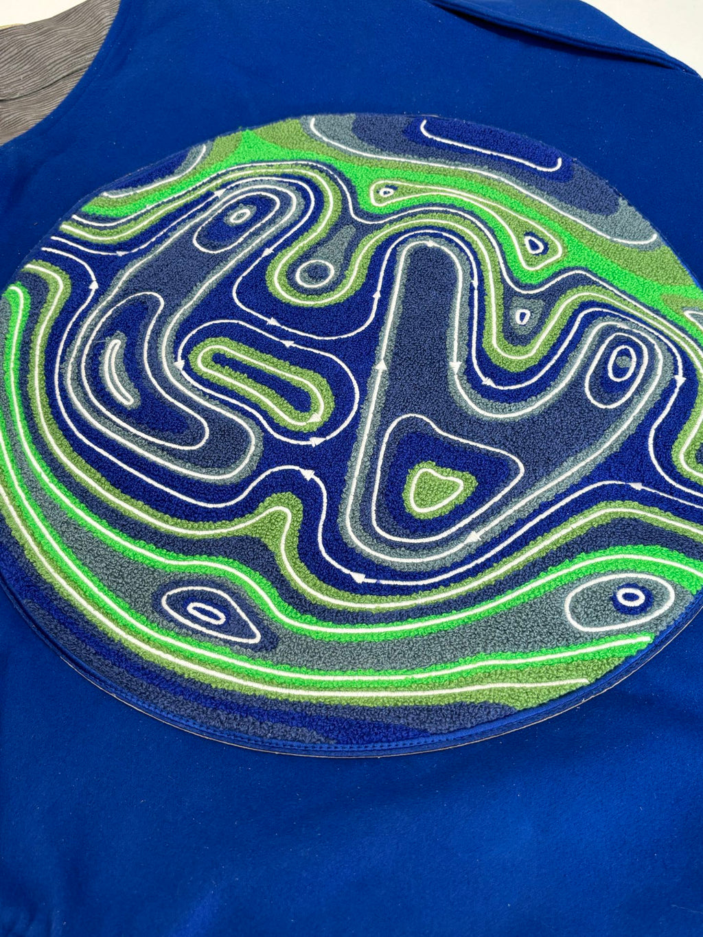 Blue varsity jacket back patch close-up with neon maze swirl graphic