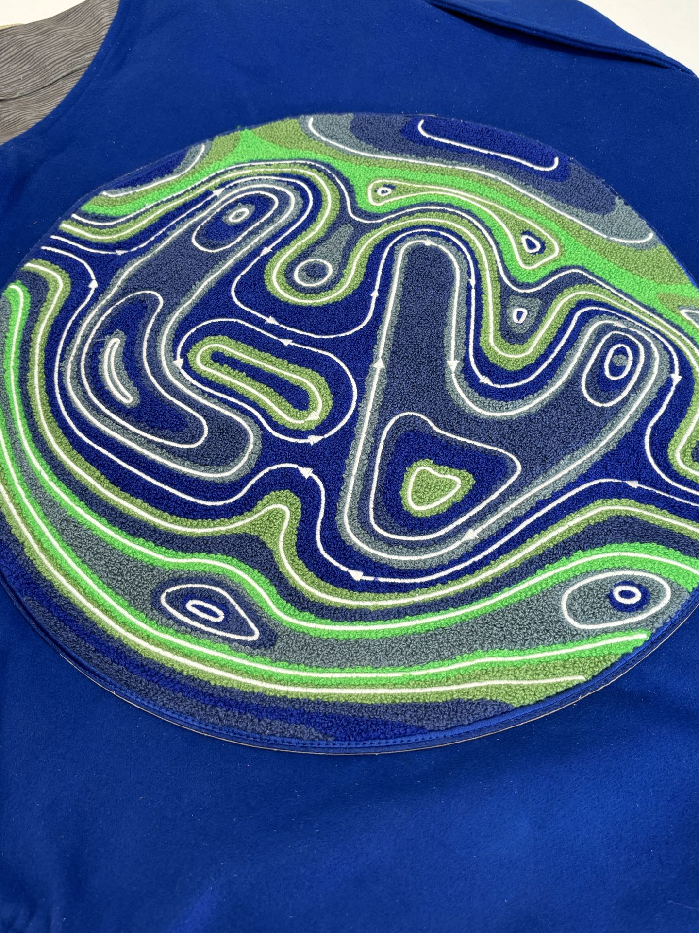 Blue varsity jacket back patch close-up with neon maze swirl graphic