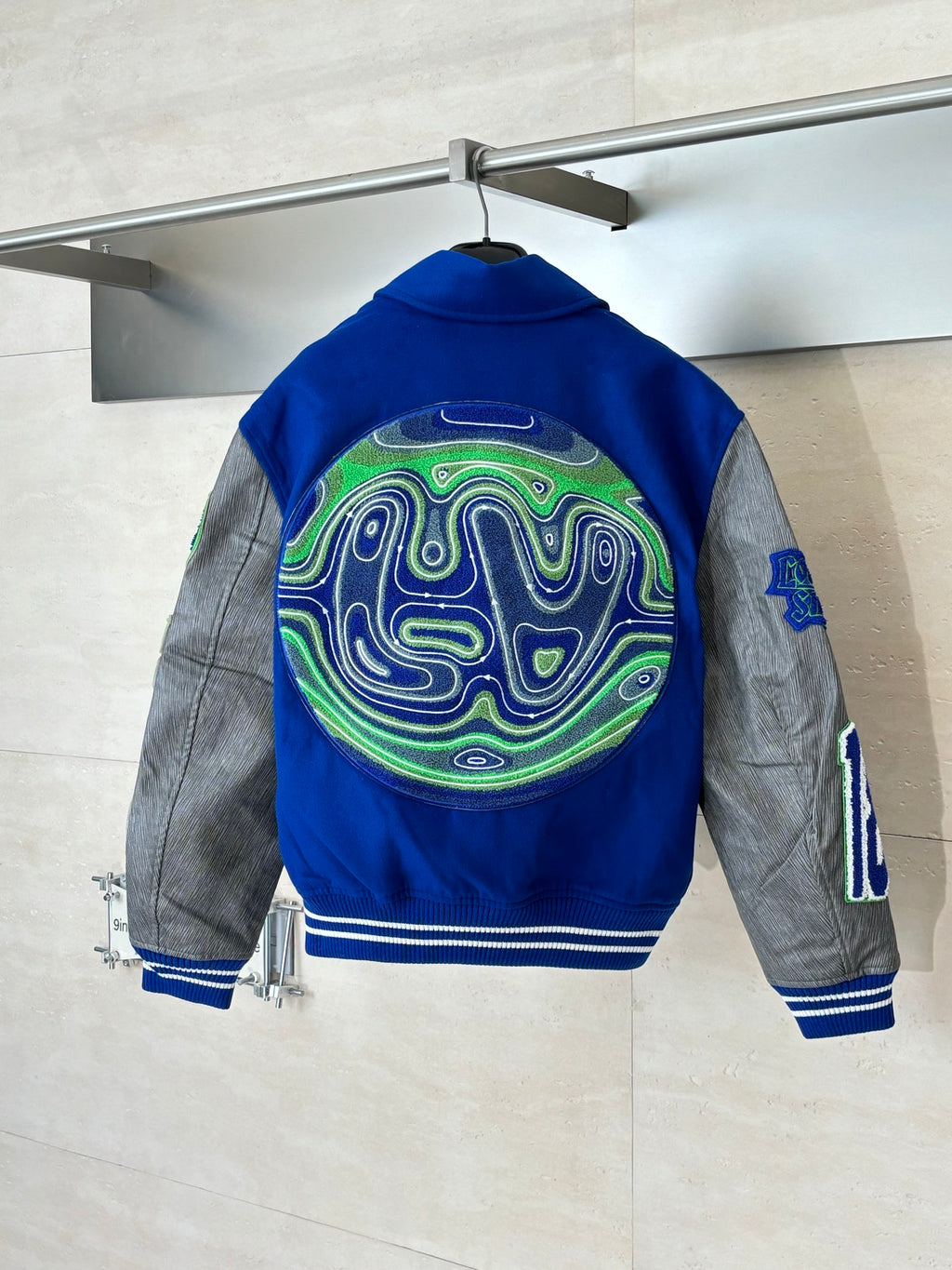 Blue varsity jacket with neon maze logo on back, gray sleeves, ribbed hem