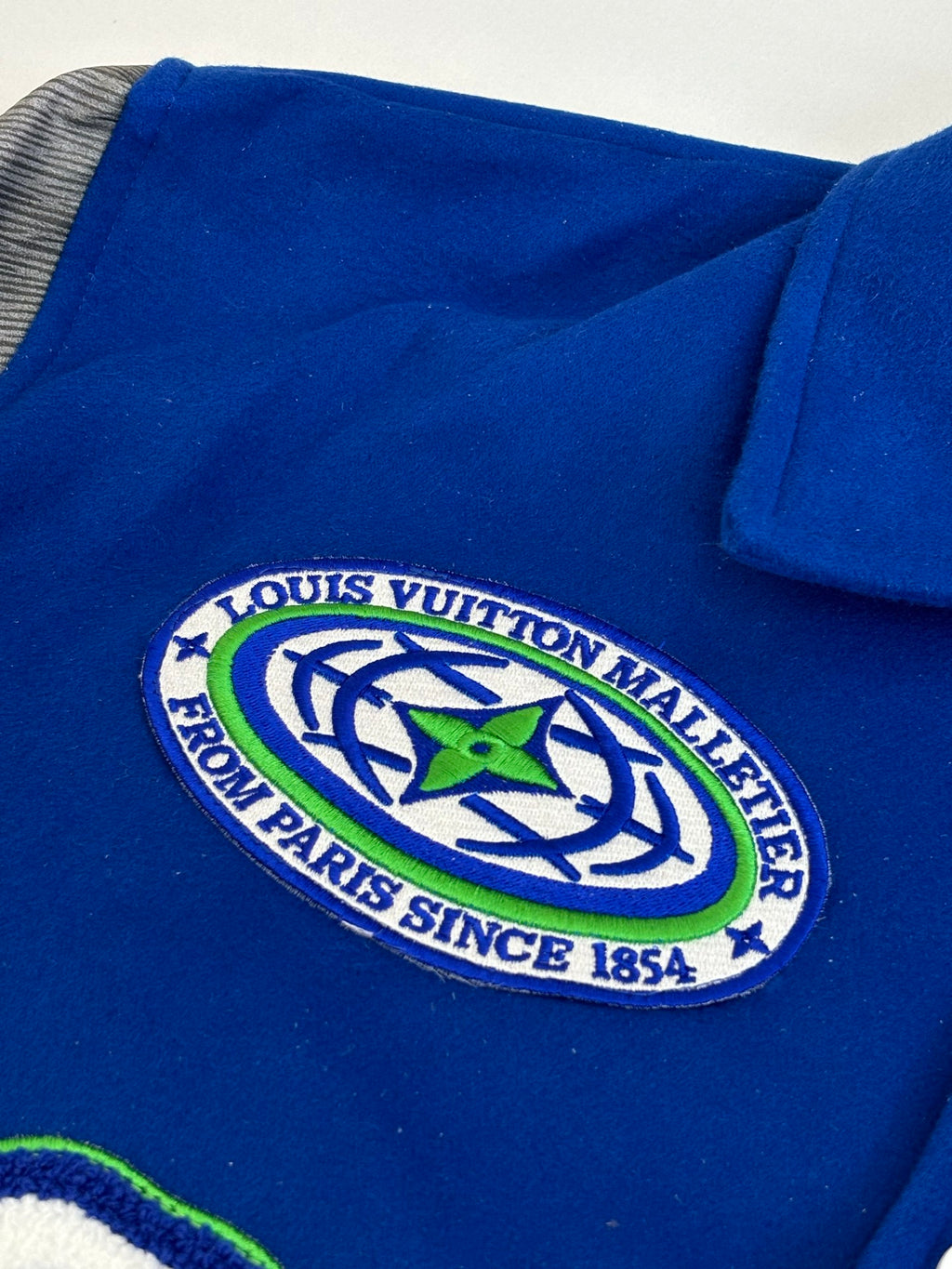 Blue varsity jacket with Louis Vuitton crest patch, white snap buttons, ribbed trim