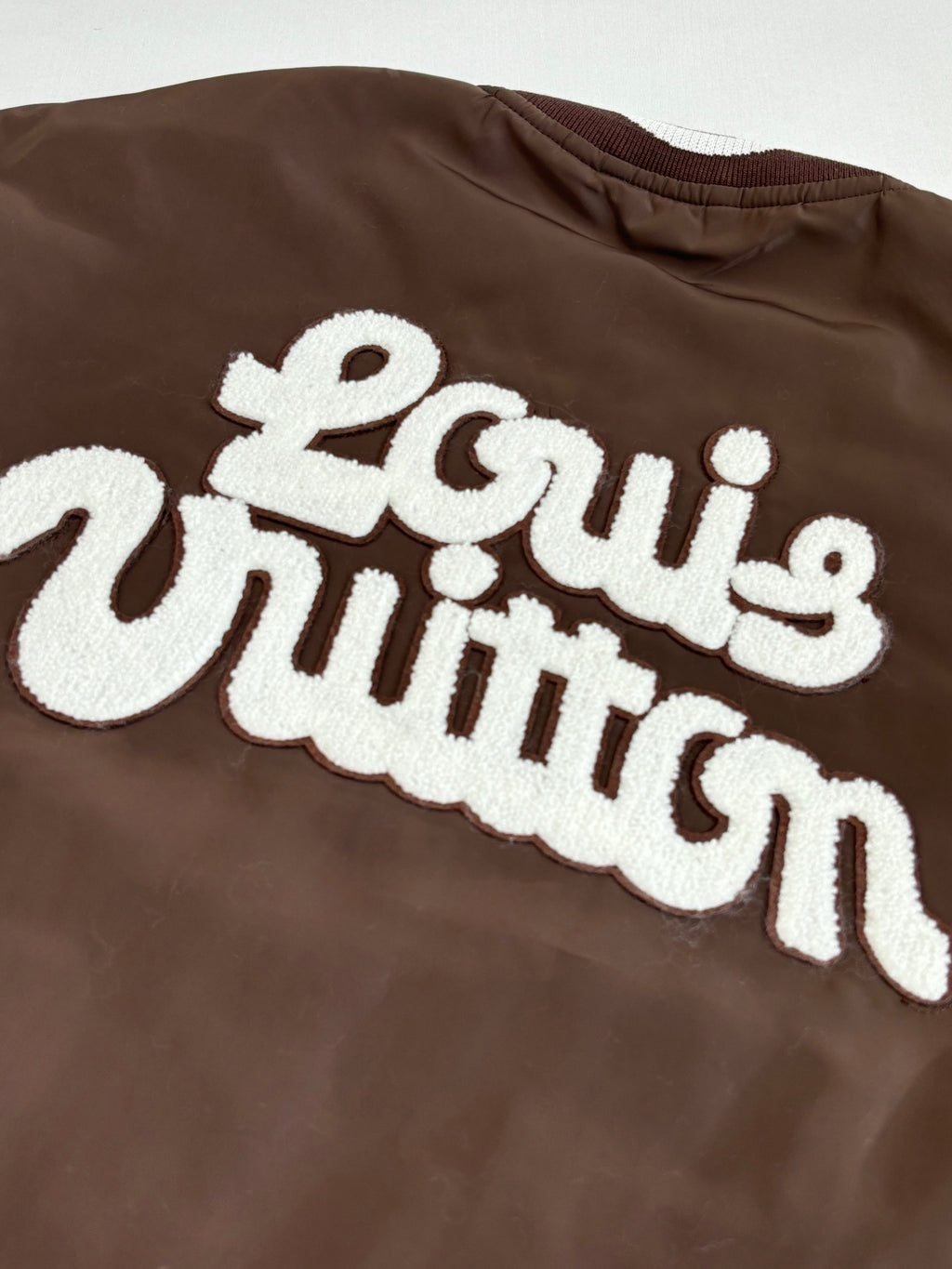 Louis Vuitton long jacket chest close-up with large white embroidered “Louis Vuitton” lettering