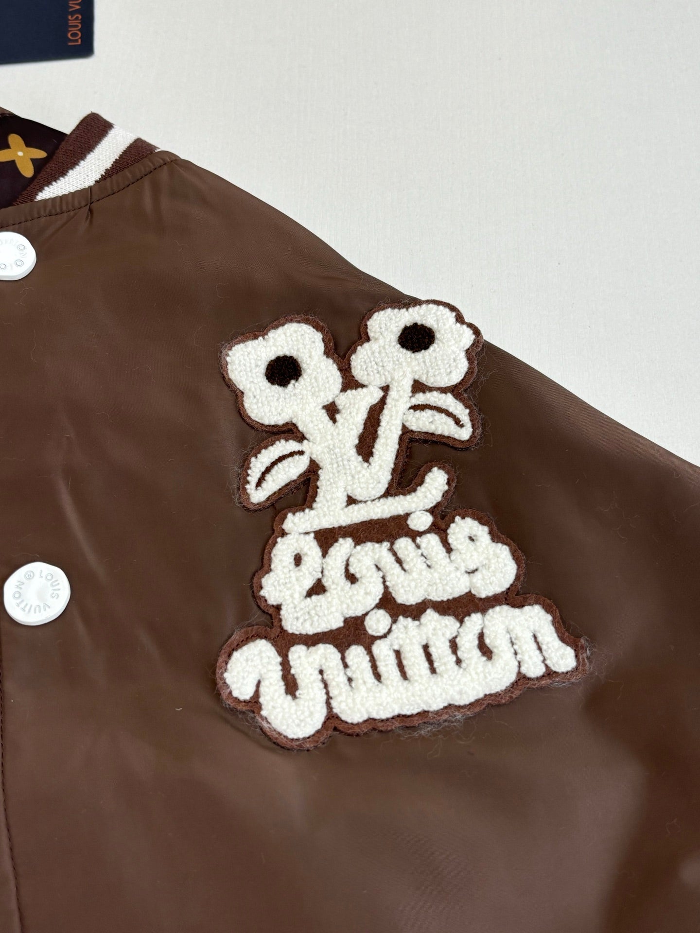 Louis Vuitton long jacket chest with embroidered white logo patch on brown fabric