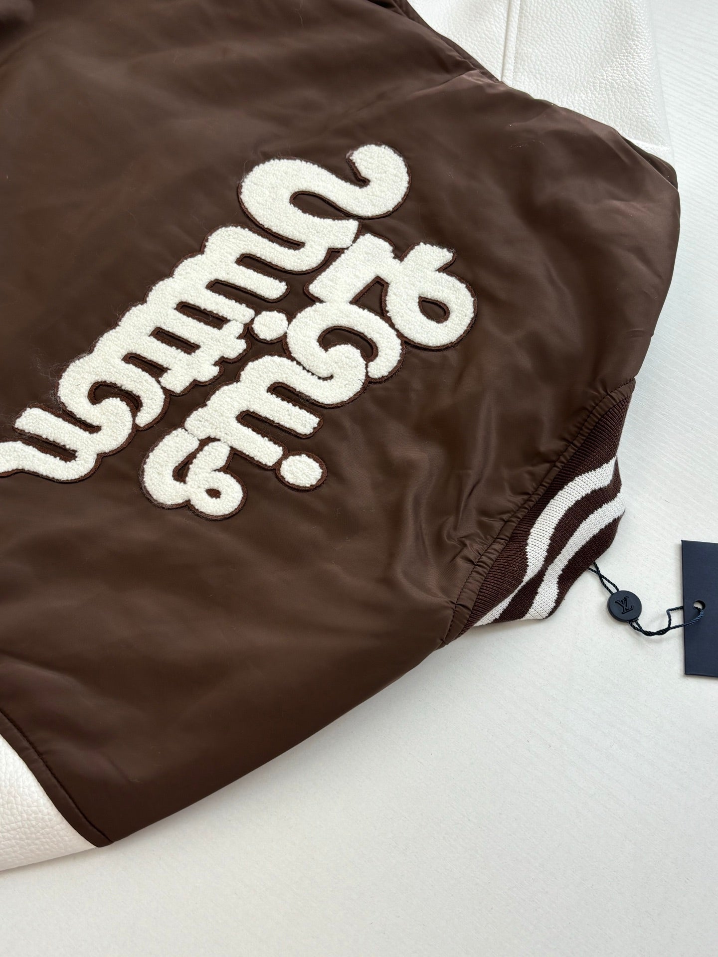 Louis Vuitton brown long jacket back close-up with white “Louis Vuitton” embroidered text