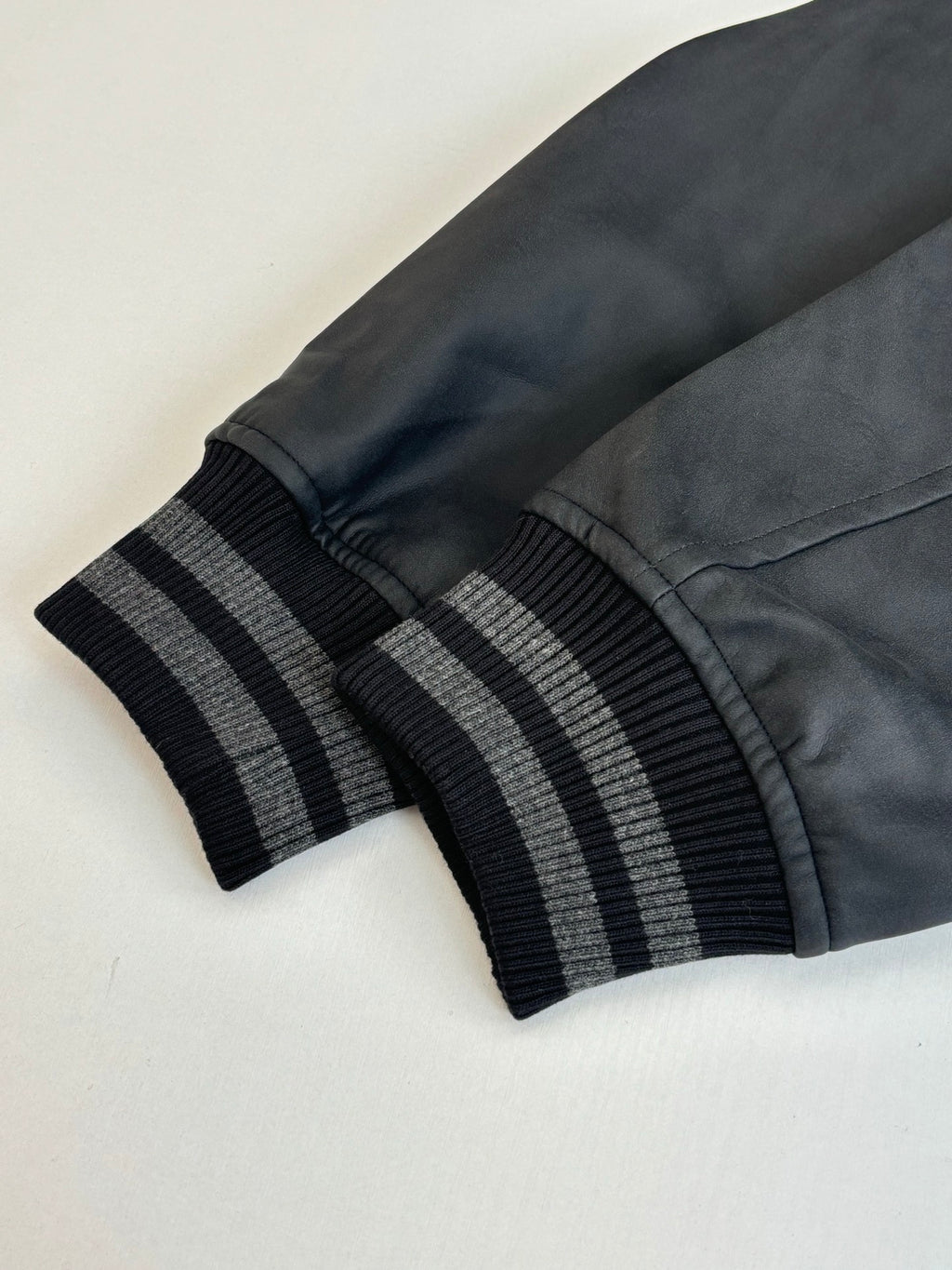 Black faux-leather sleeve with dark ribbed striped cuff on gray varsity jacket