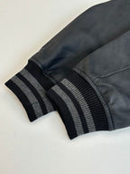 Black faux-leather sleeve with dark ribbed striped cuff on gray varsity jacket