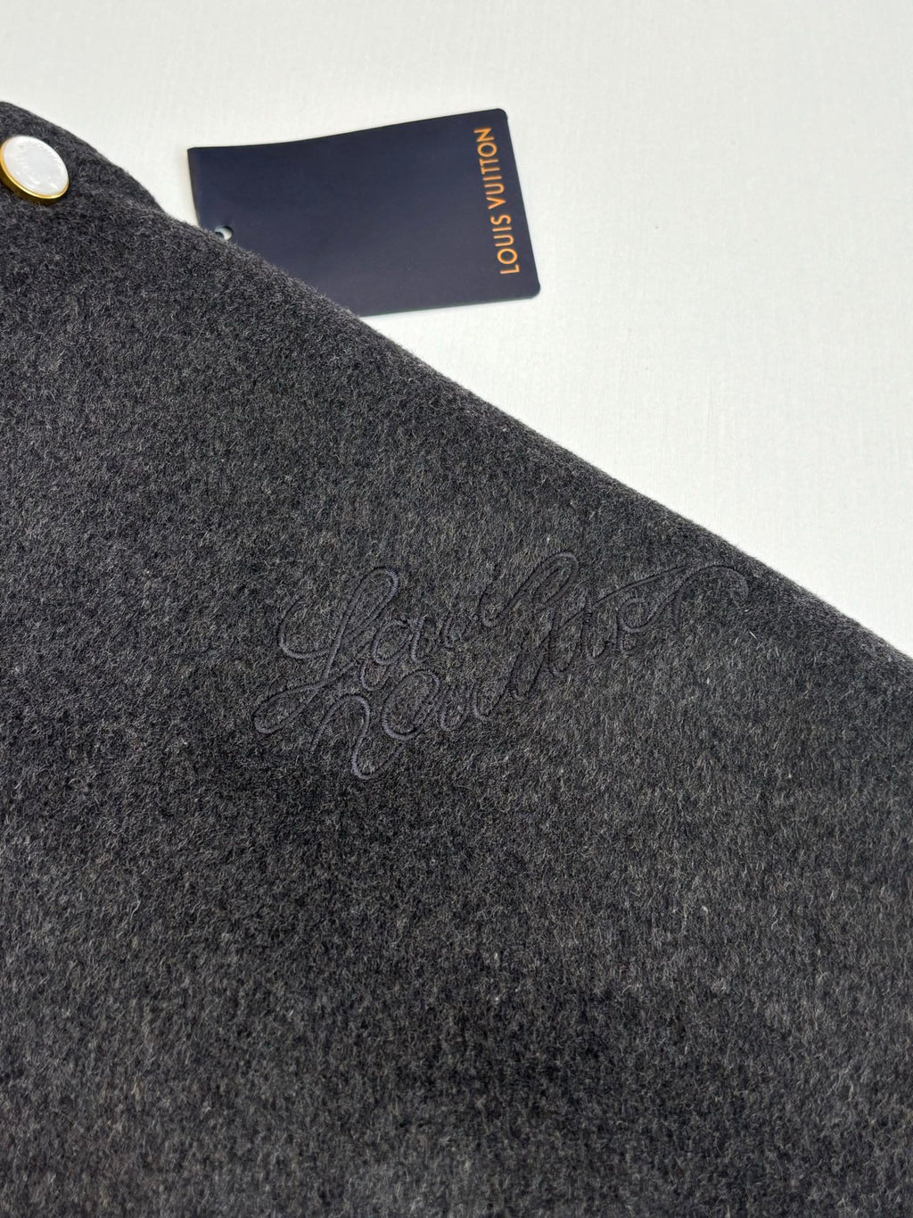 Dark gray textured wool varsity jacket fabric with embossed signature detail